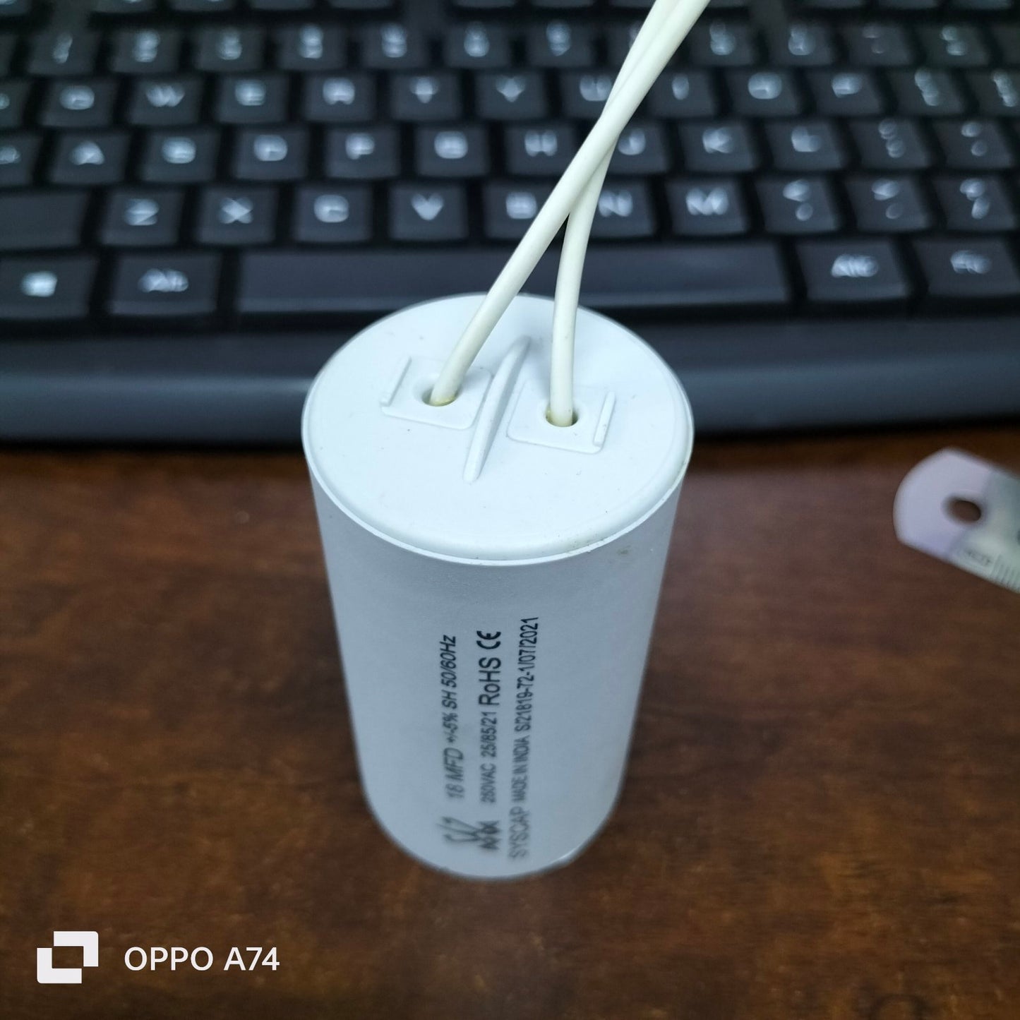 Syscap 18MFD 250 VAC Running Capacitor with white wires on a wooden surface near keyboard
