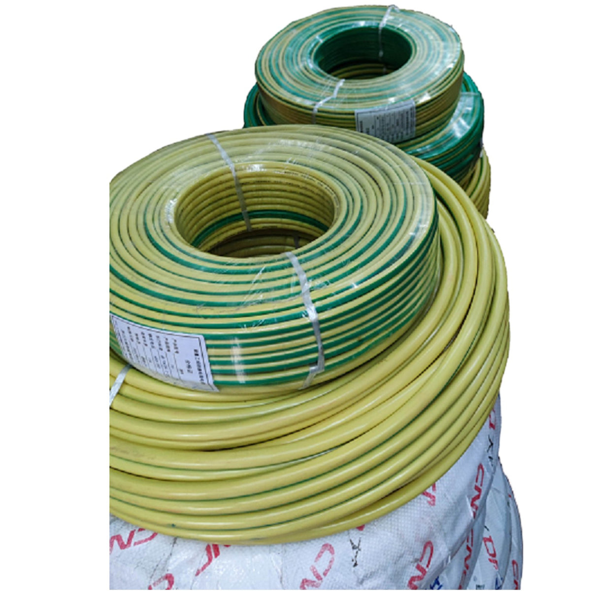 Three coiled rolls of yellow and green electrical wire or cable, wrapped in clear plastic and secured with white straps, stacked on top of a white woven bag against a plain white background.