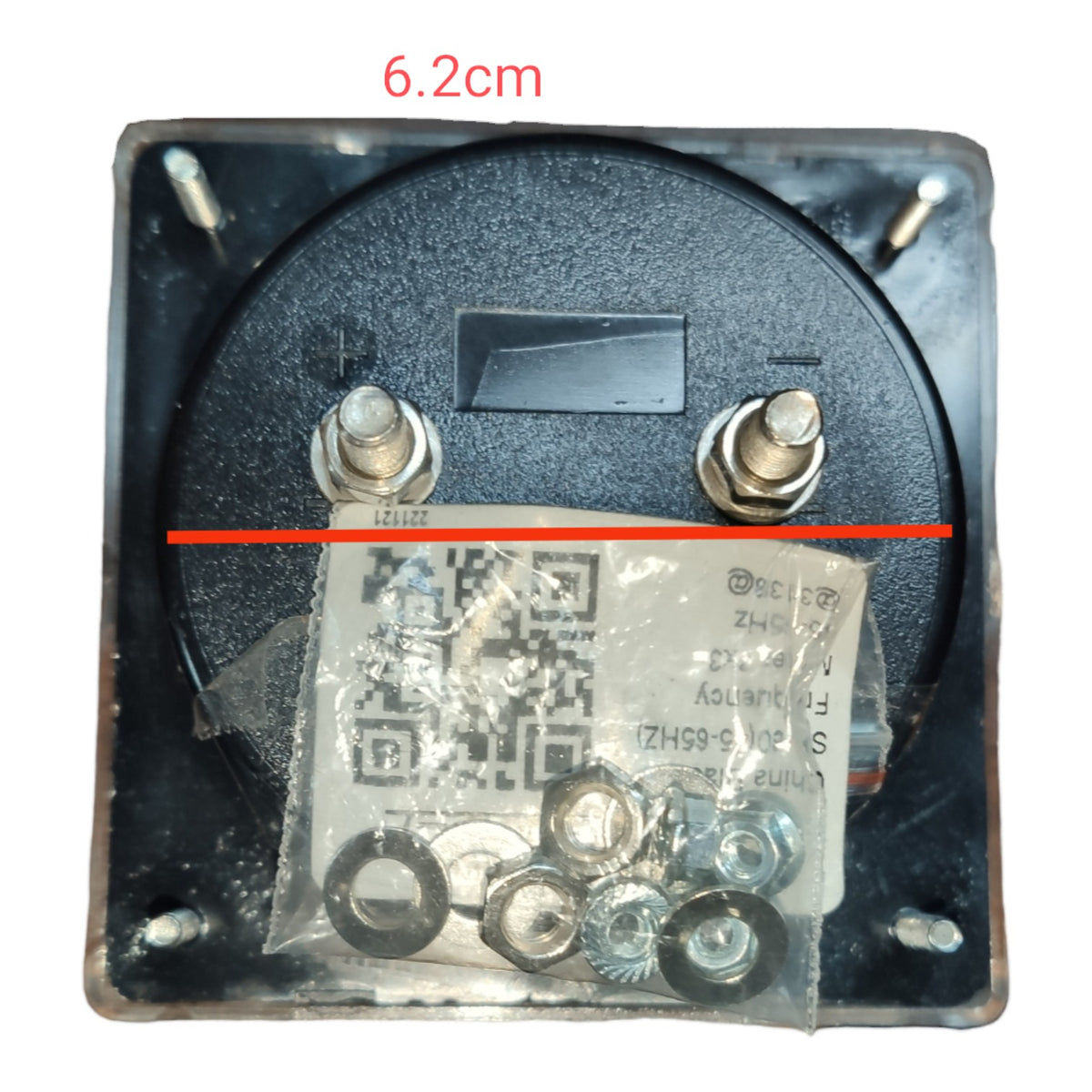 A square black electronic component or enclosure with a circular insert, two metal terminal screws, and a clear plastic bag containing small hardware pieces. A red measurement overlay reads 6.
