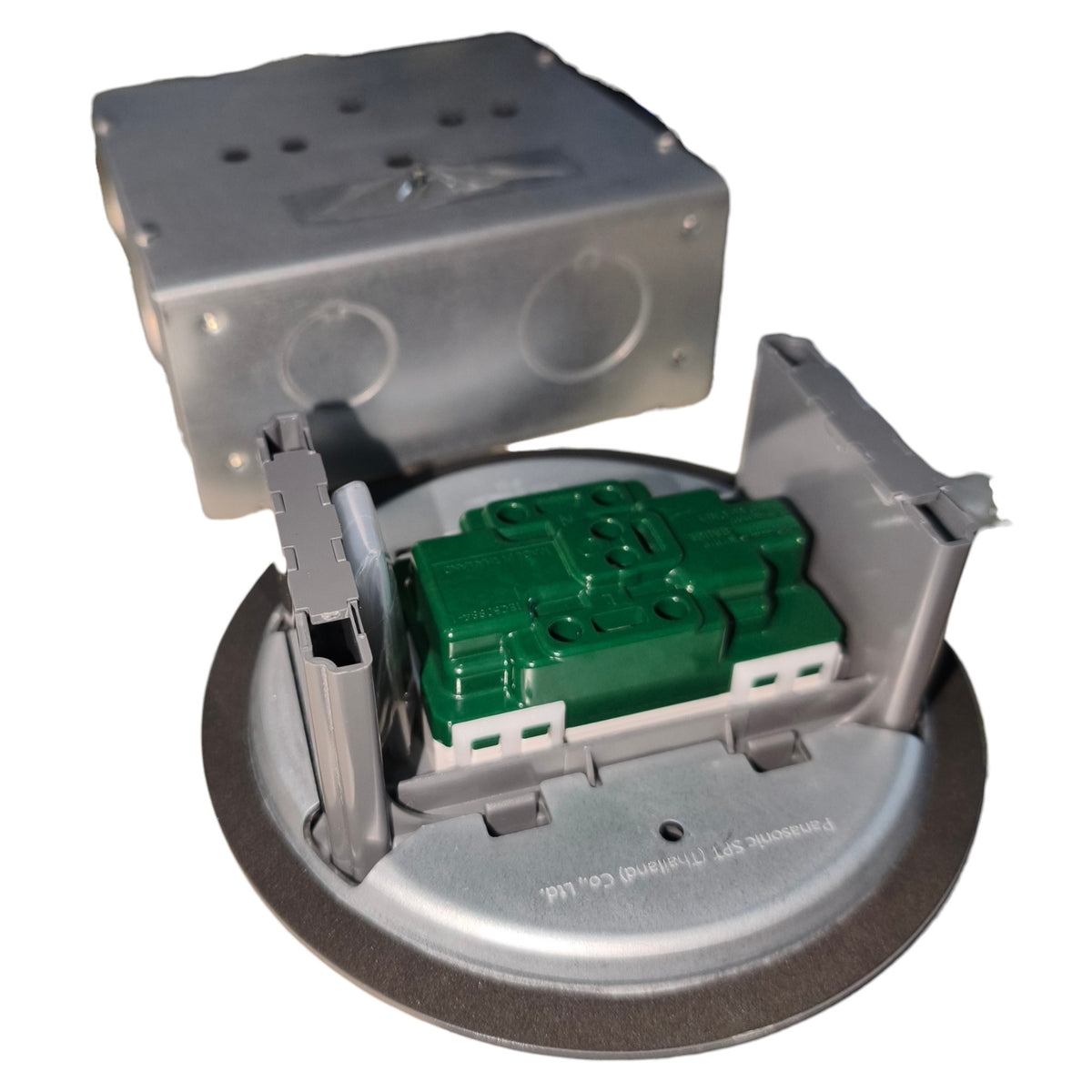 A circular metal electrical component with a green plastic module in the center, shown with its upper metal cover removed and set against a plain white background.