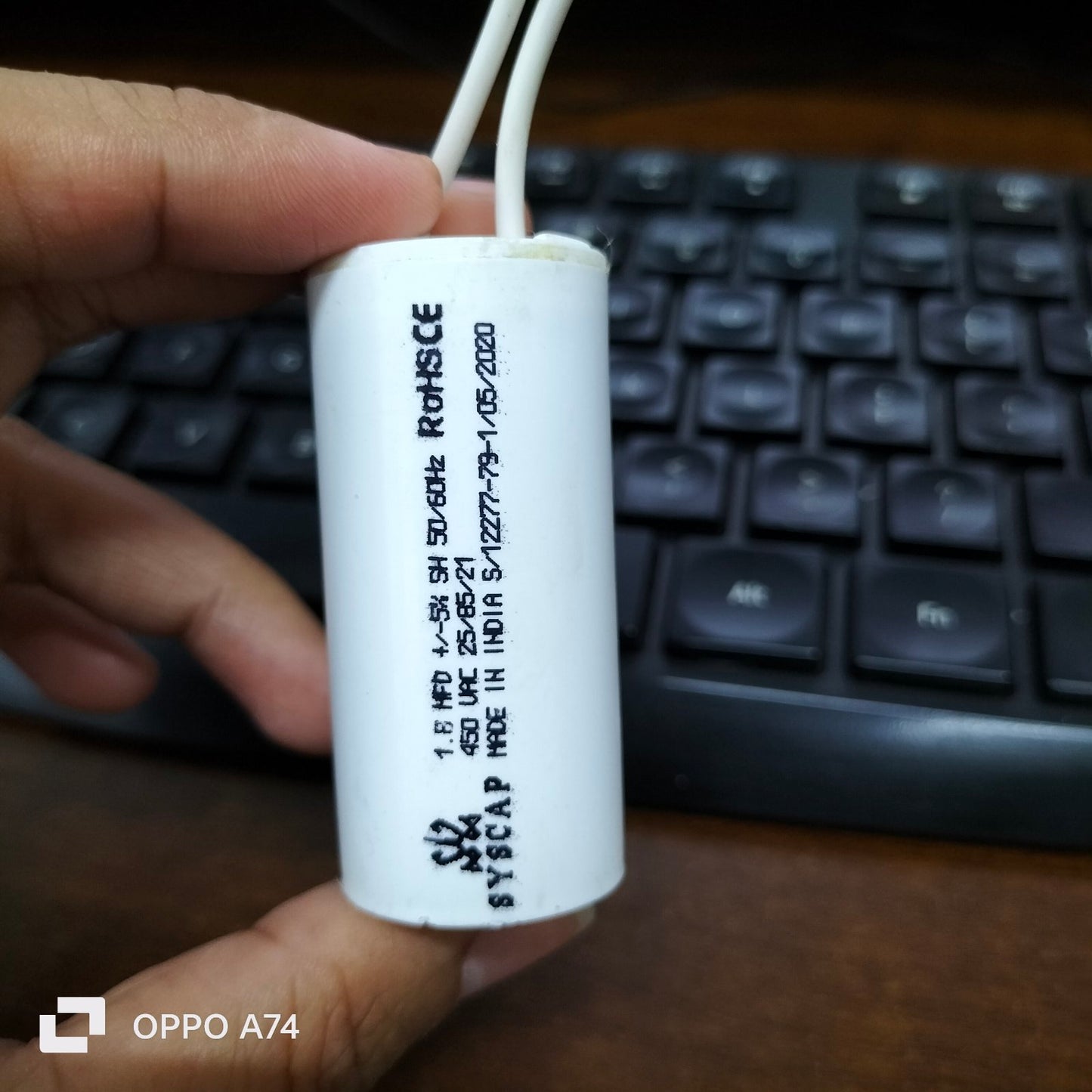 Syscap 1.8MFD 450V AC Motor Running Capacitor held in hand with keyboard background