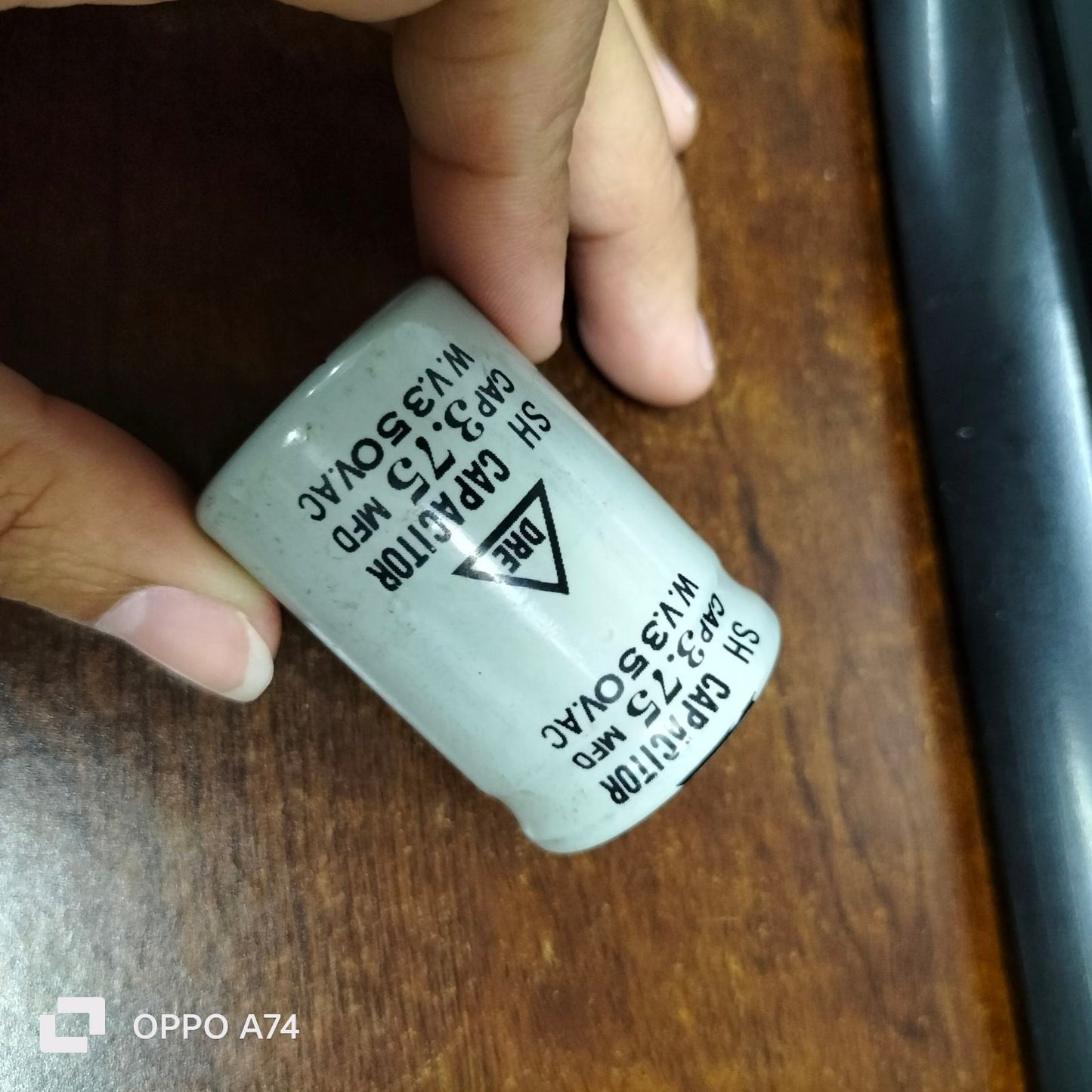 DRE 3.75 MFD motor running capacitor held by hand on wooden surface