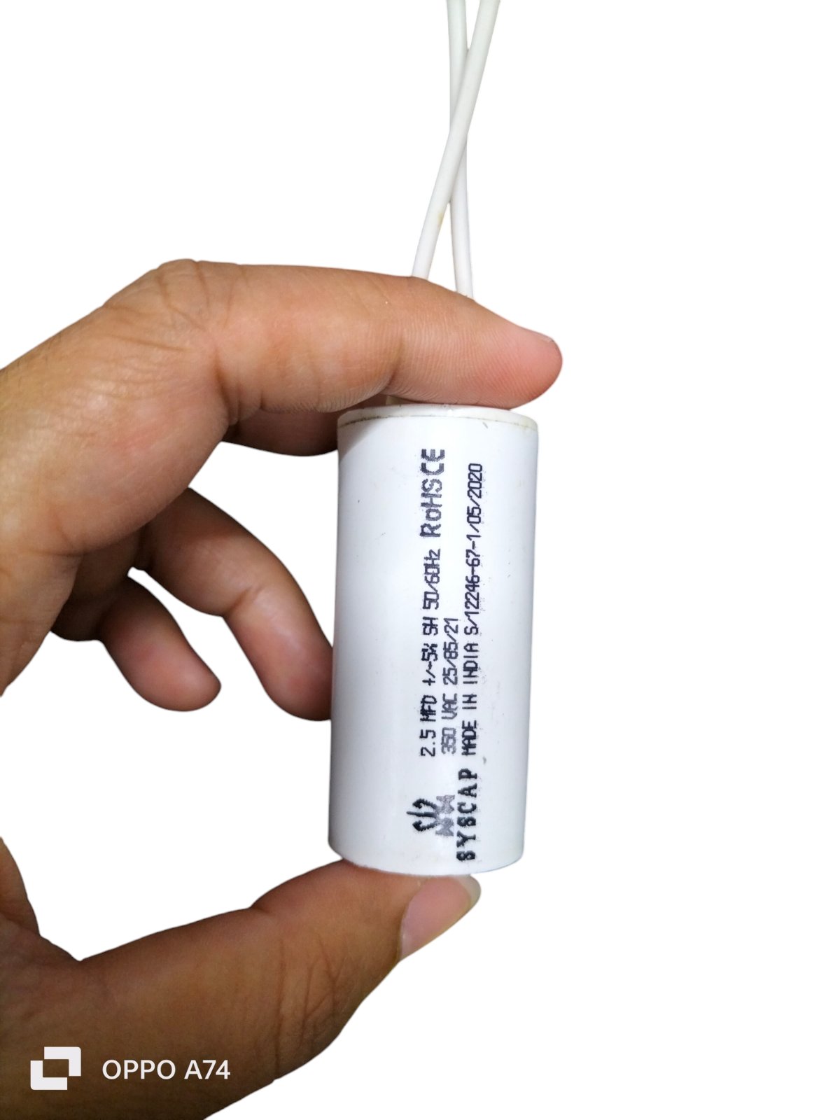 Hand holding a Syscap Motor Running Capacitor 2.5MFD white cylindrical electrical component with wires