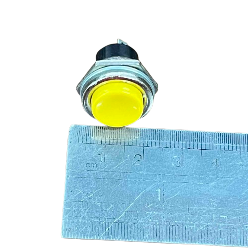 Push Button Switch 1A 220V Yellow with a shiny surface on a measurement ruler