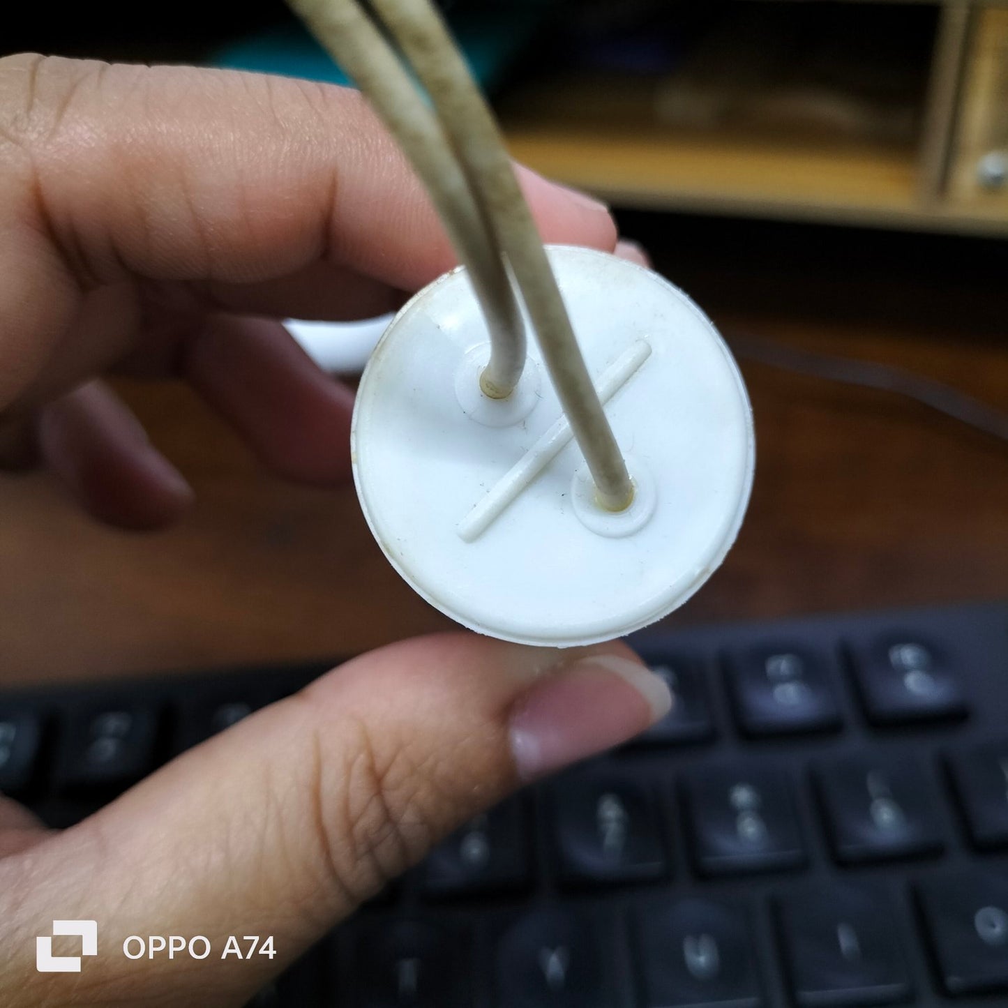 Close-up of SYSCAP 1.5 microfarad capacitor held by hand showing white cylindrical electrical part with attached wires