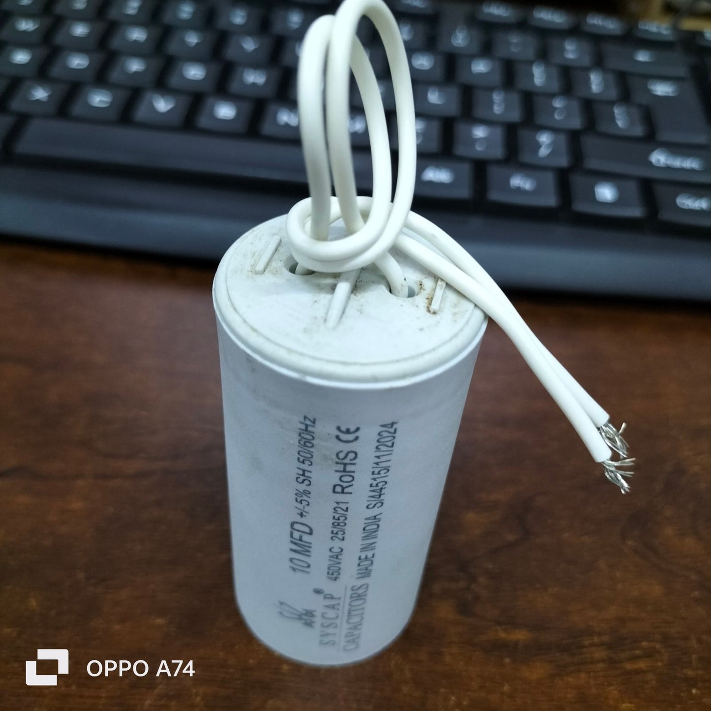 Syscap 10MFD 450 VAC Running Capacitor with white wires on a wooden surface near keyboard