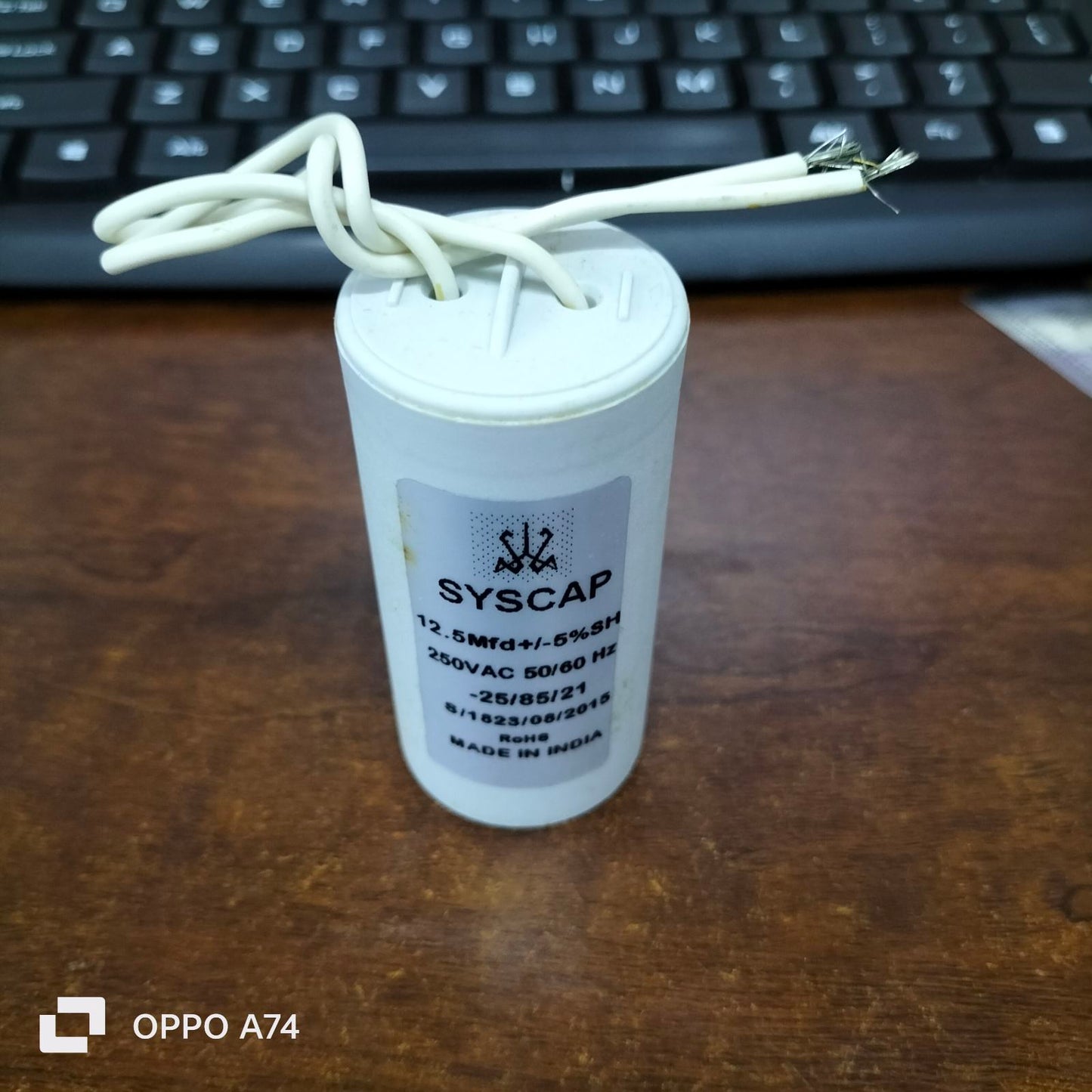 Syscap 12.5MFD 250 VAC Running Capacitor with white wires on wooden surface near keyboard