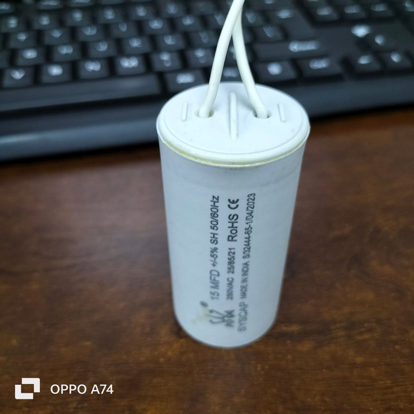 Syscap 15MFD 250V AC Running Capacitor with white cylindrical body and attached wires on wooden surface