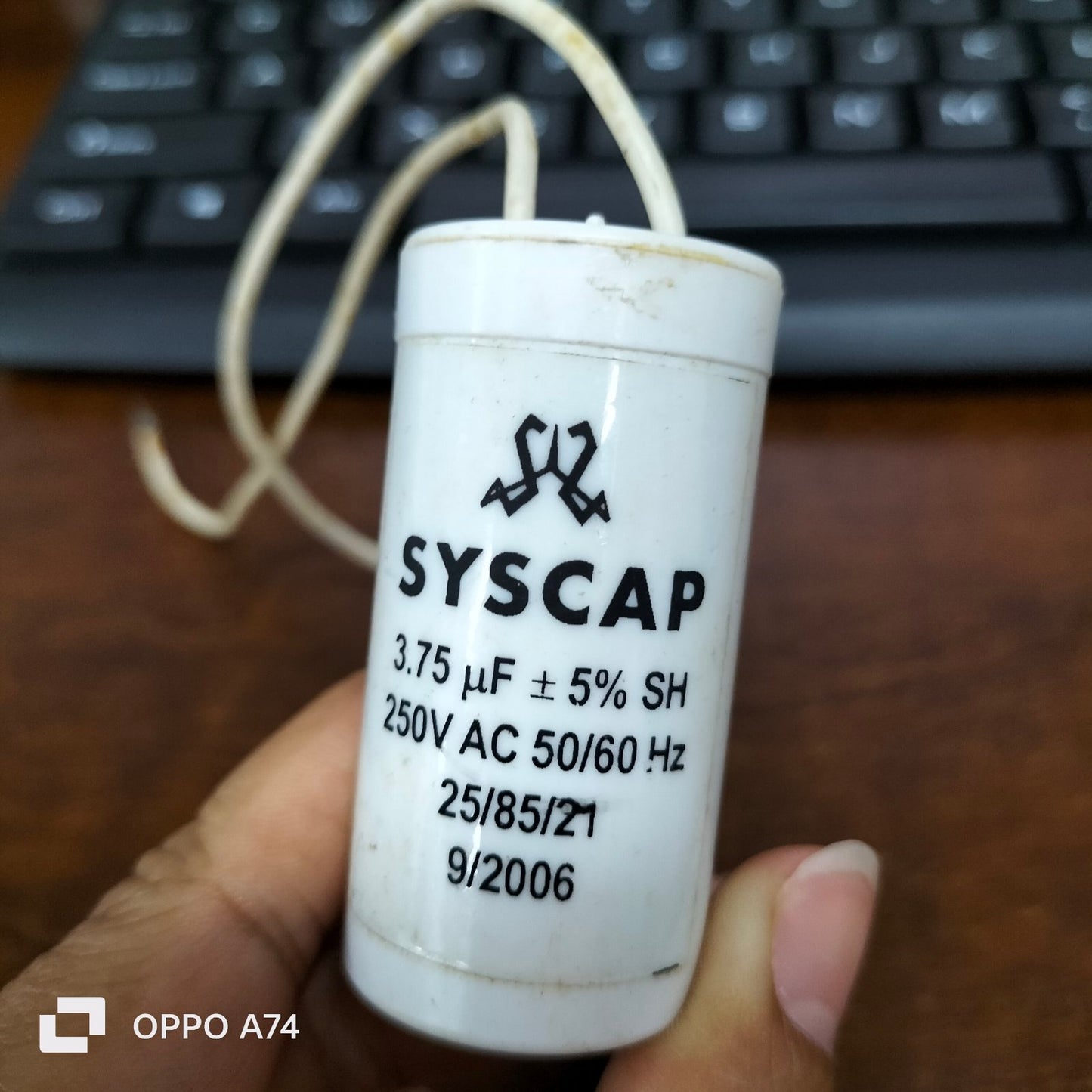 Syscap 3.75uF 250V AC capacitor held in hand with printed specifications on white cylindrical body