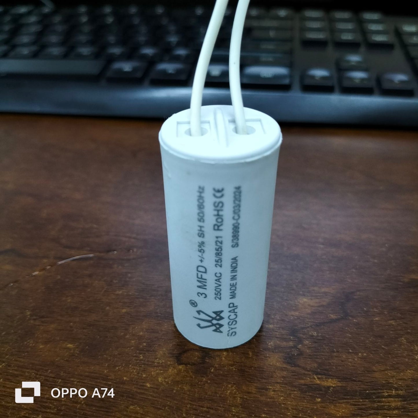 Syscap 3MFD 250 VAC Running Capacitor electrical component with white wires on wooden surface