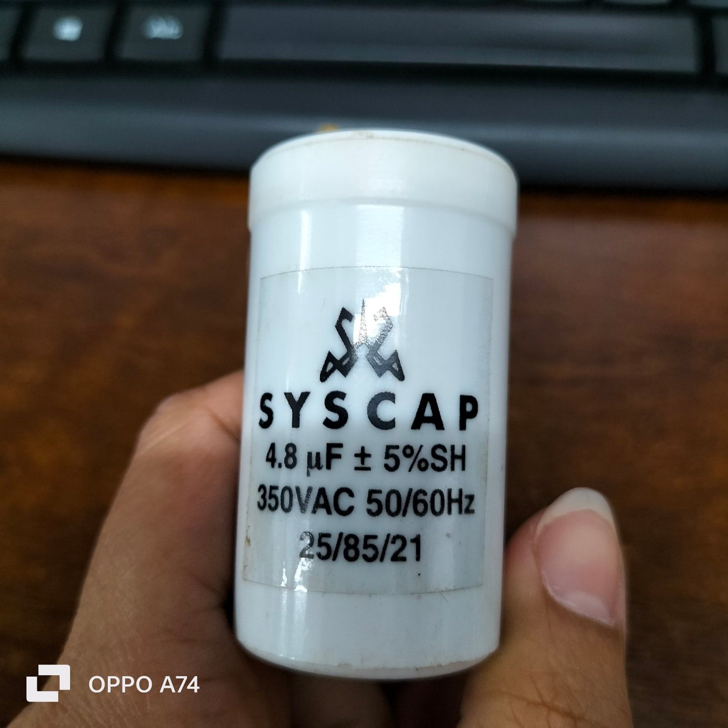 Syscap 4.8 microfarad 350V AC capacitor held between fingers with keyboard background