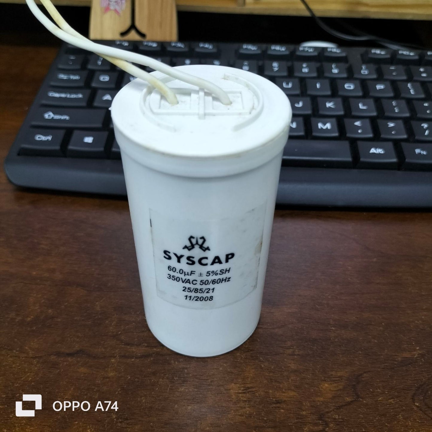 Syscap 60MFD 350V AC Running Capacitor with white cylindrical body and attached wires on wooden desk