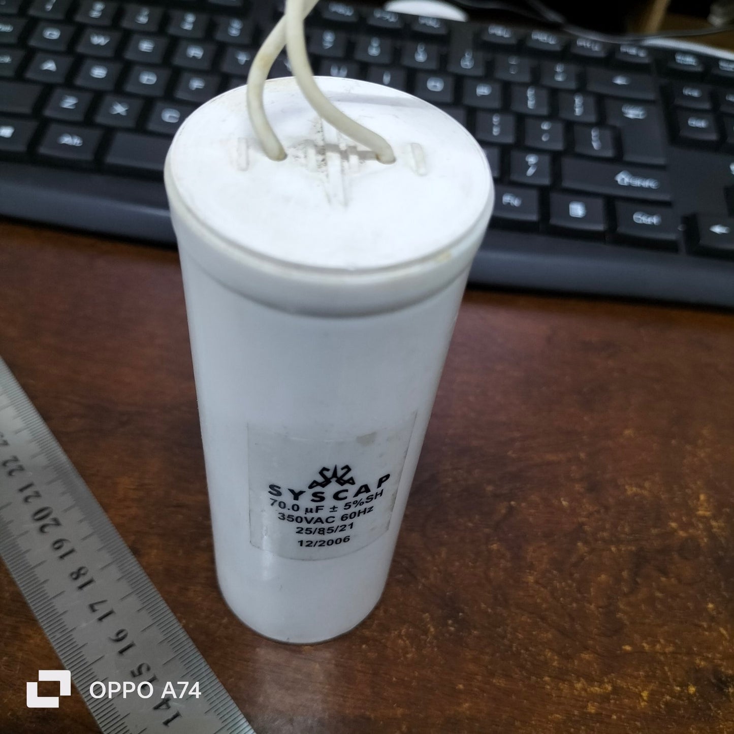 Syscap 70MFD 350 VAC Running Capacitor electrical component with wires on wooden surface next to ruler