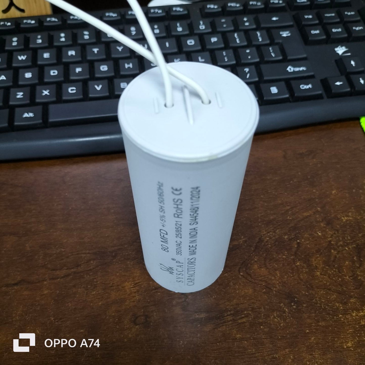 Syscap 80MFD 350V ACRunning Capacitor with white wires on a wooden desk near a black keyboard