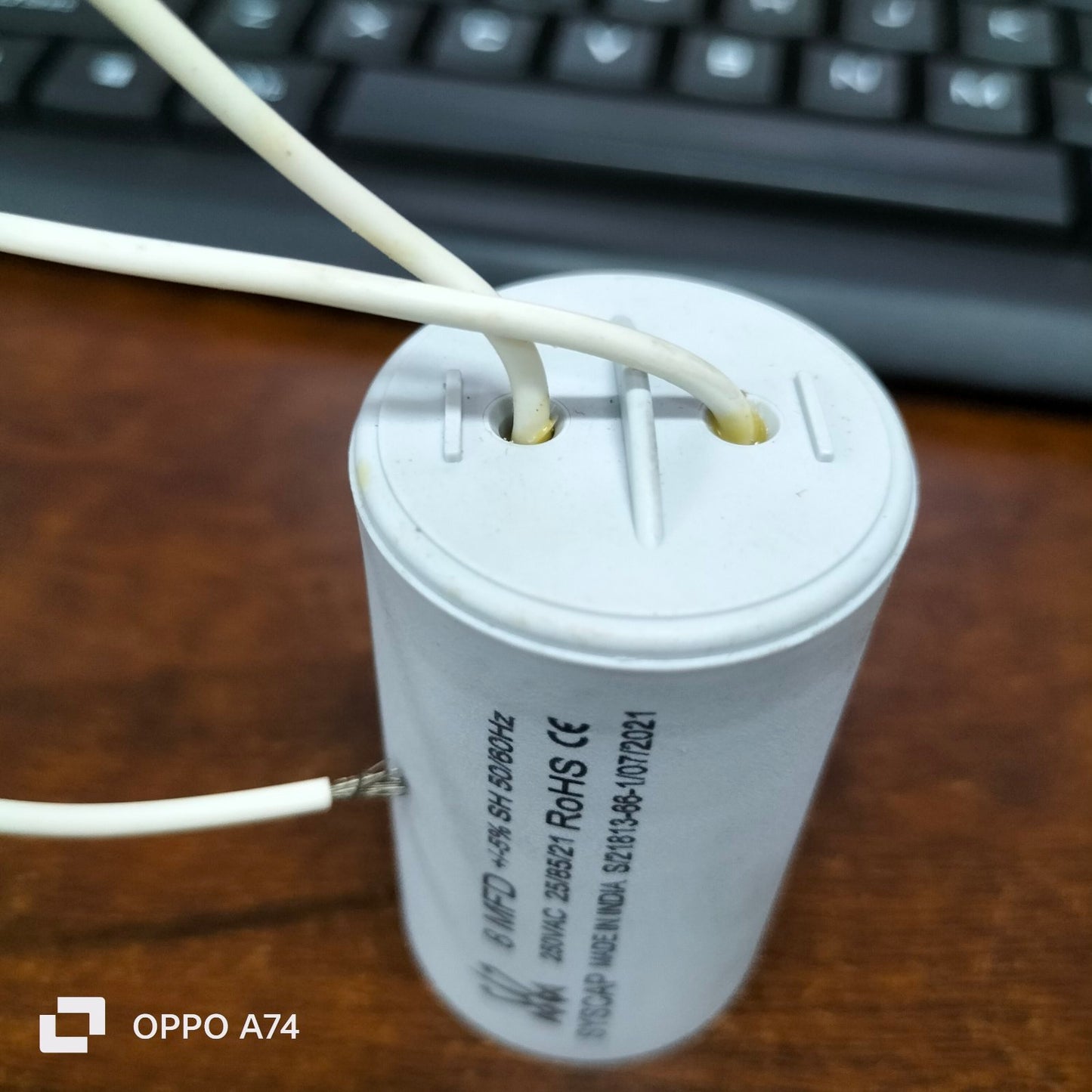 Syscap 8MFD 250 VAC Running Capacitor electrical component with white wires on wooden surface