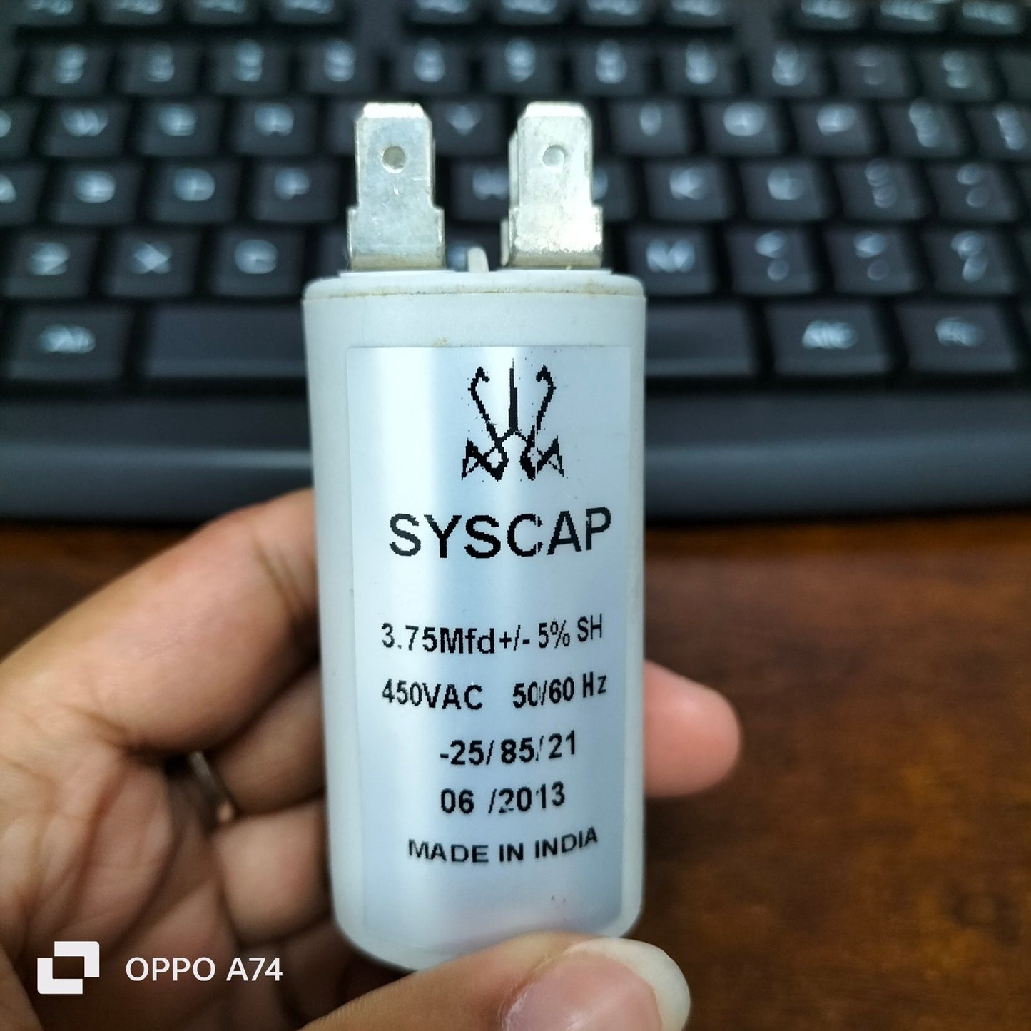 SYSCAP motor capacitor 3.75MFD white cylindrical electrical part held in hand with black keyboard background