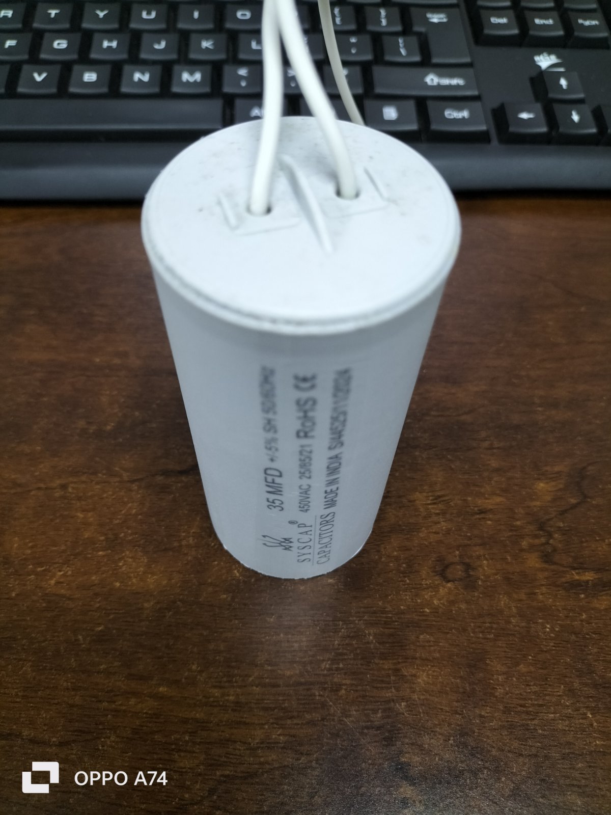 Syscap motor capacitor with white cylindrical body and two attached wires