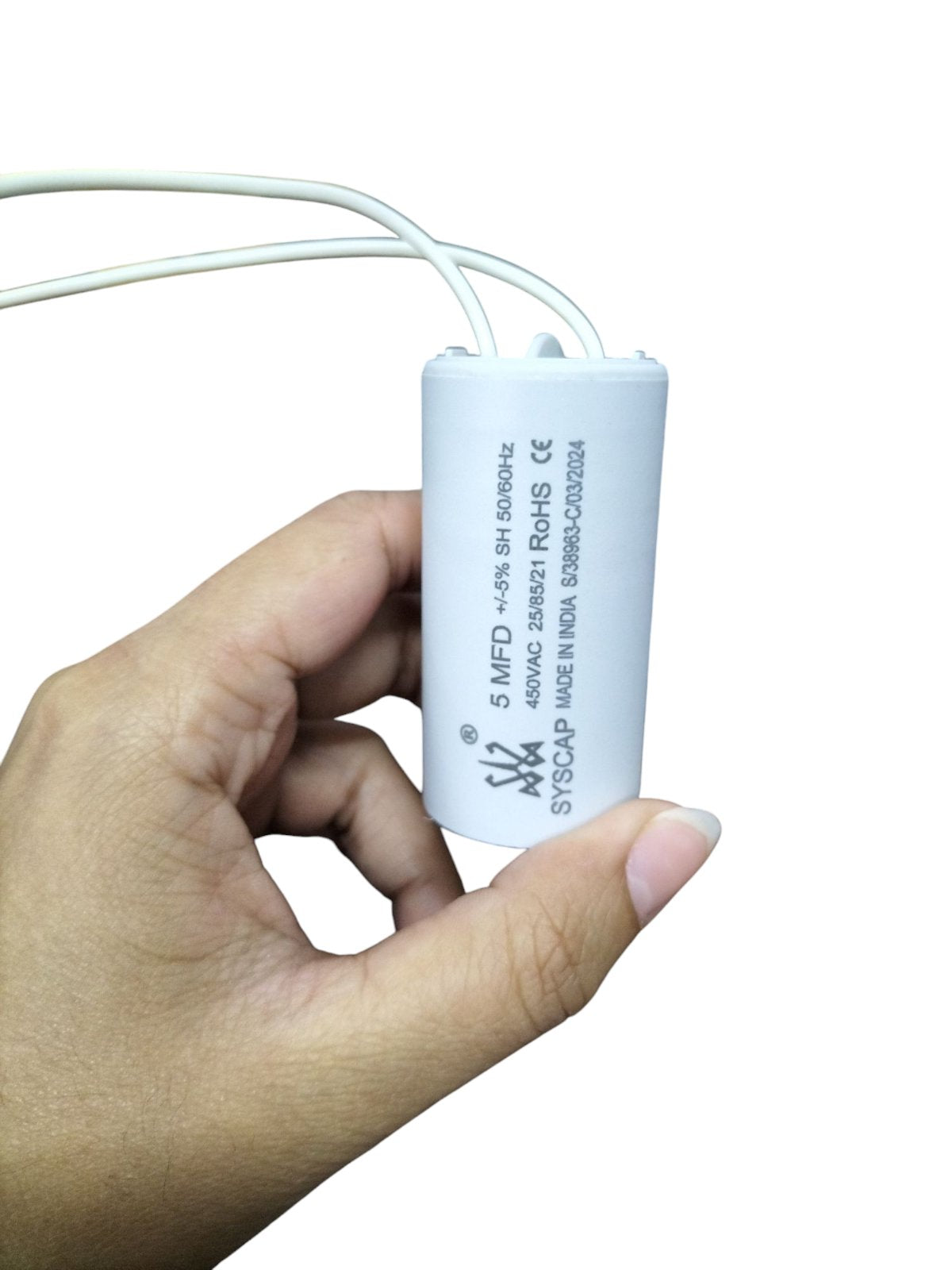 Hand holding a white SYSCAP motor capacitor 5MFD electrical component with attached wires
