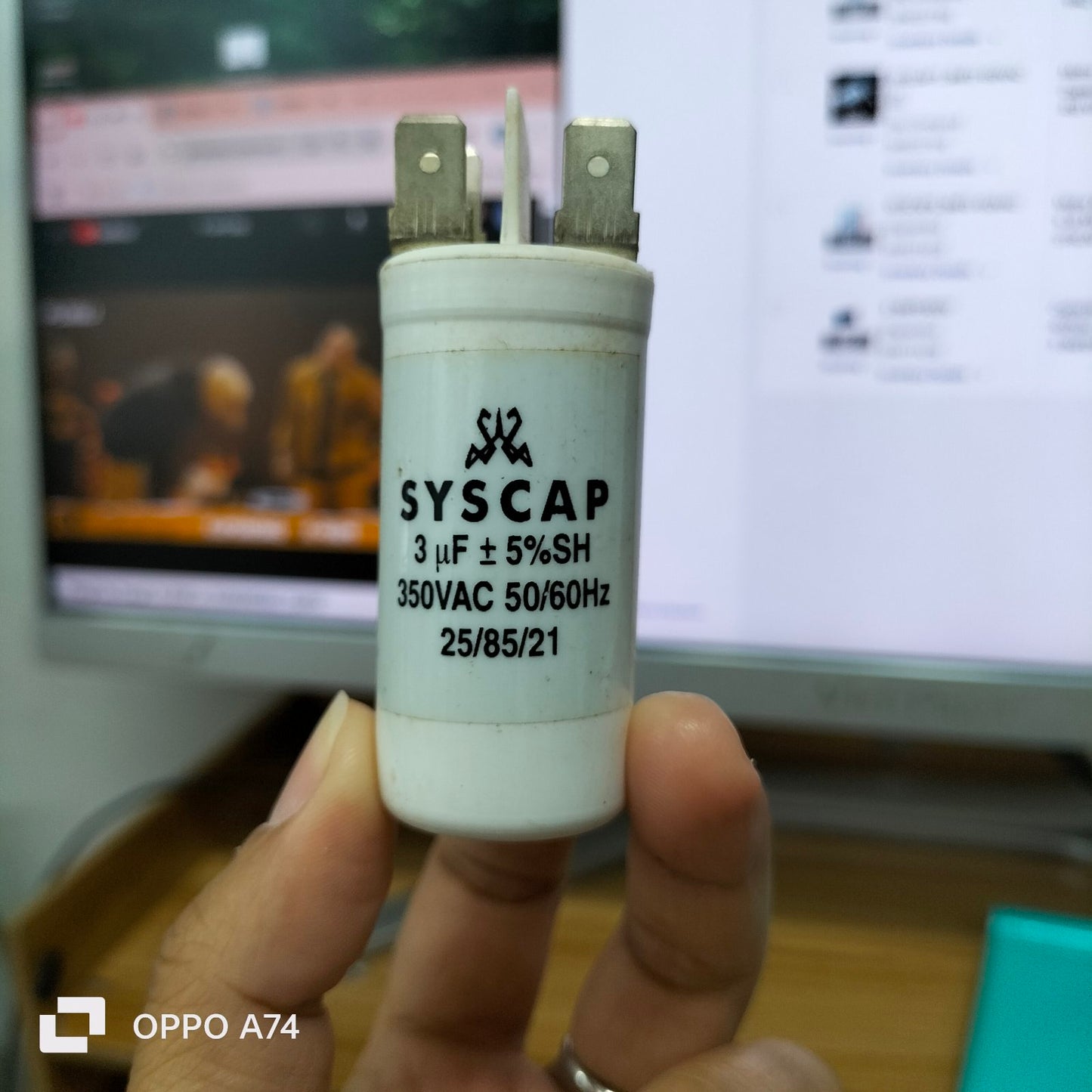 Syscap motor running capacitor 3mfd 350vac held in hand with white cylindrical body and metal terminals
