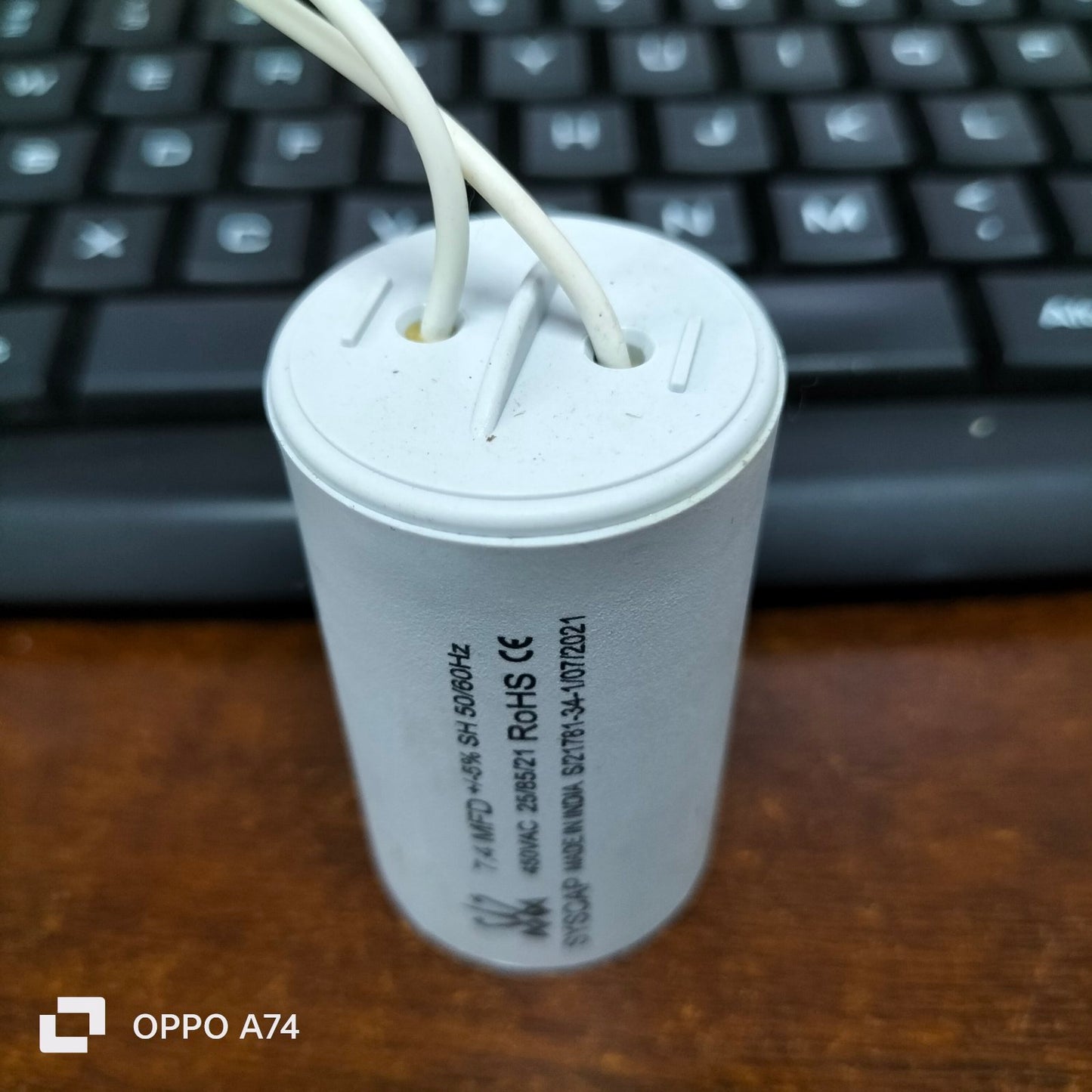 Syscap electrical Running Capacitor 7.4MFD 450 VAC with white wires on a wooden surface near keyboard