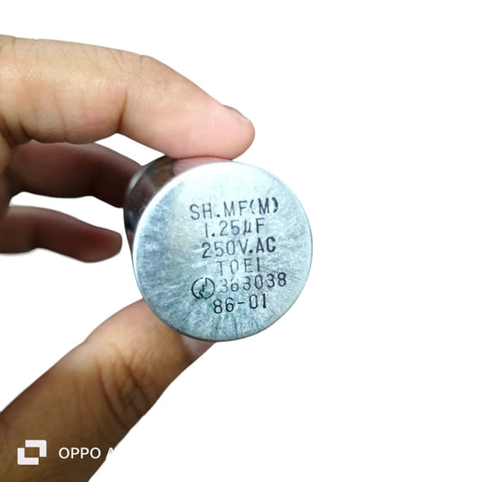 Hand holding SH 1.25MFD 250V AC capacitor for electrical circuitry and parts