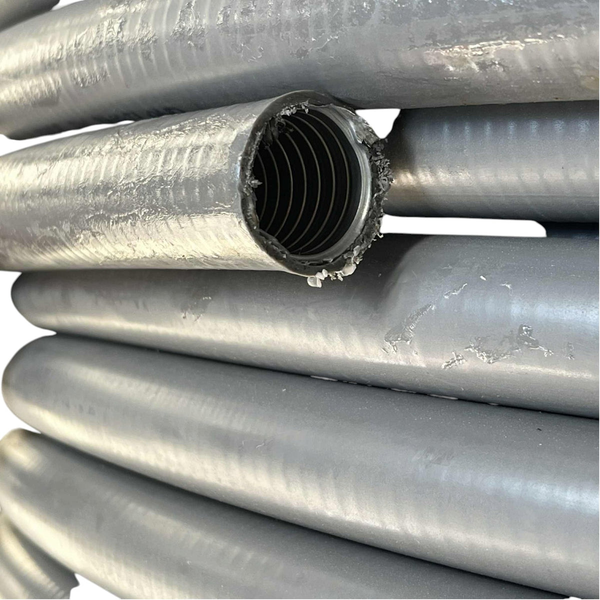 Close-up of several gray corrugated plastic pipes stacked together, with one pipe cut open to show the ribbed inner wall.