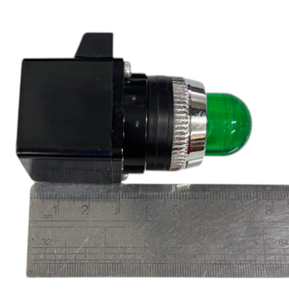 A small black electrical push-button switch with a green dome-shaped button and a silver metal ring, shown next to a metal ruler for scale on a white background.