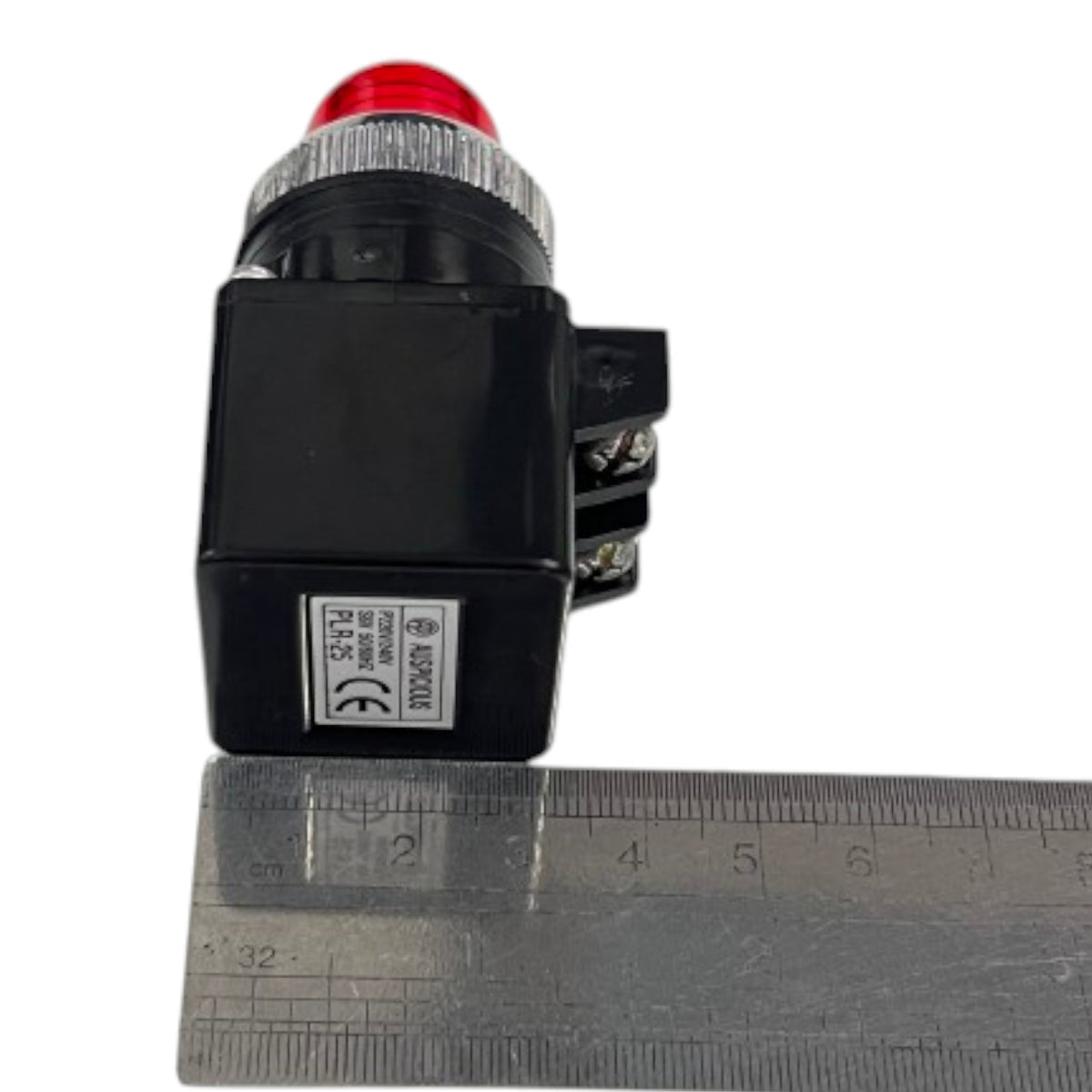 A black industrial push-button switch with a red dome top and a silver ribbed collar, shown next to a metal ruler for scale on a white background.