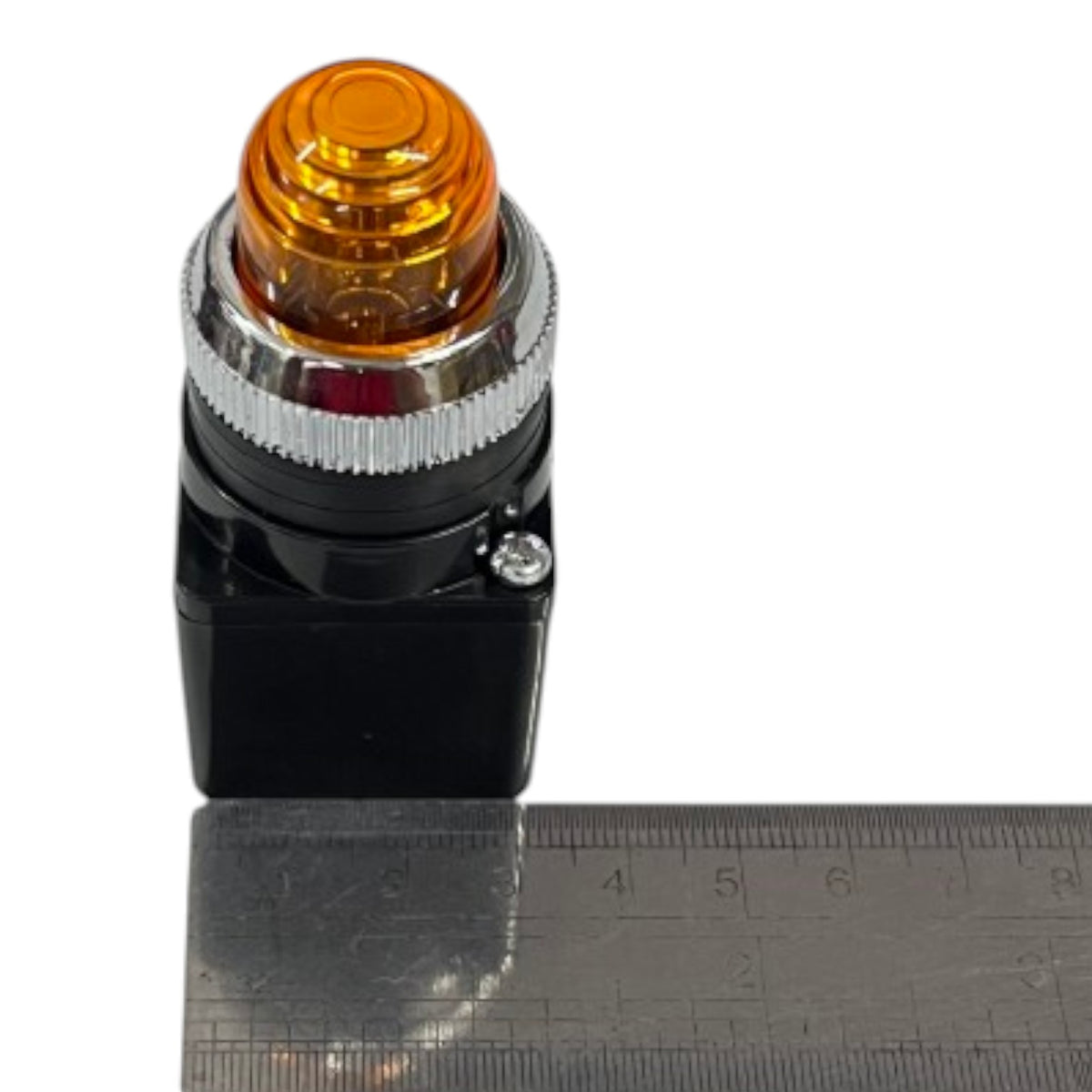An industrial-style amber warning light switch with a black base, silver metal collar, and clear amber lens, shown next to a metal ruler for scale on a white background.