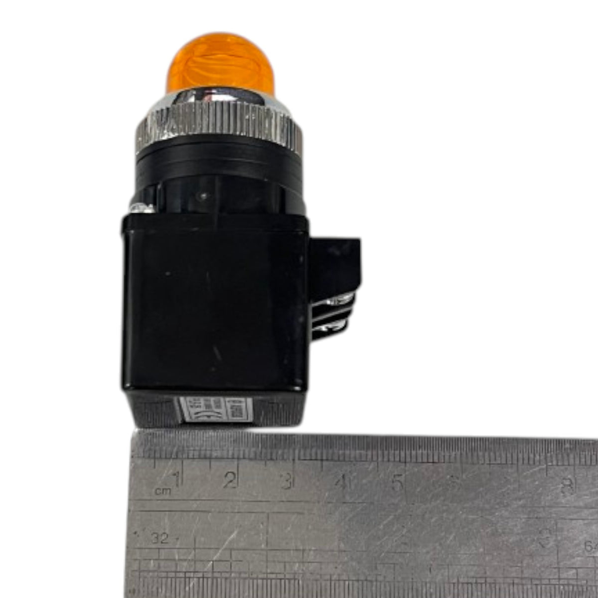 A small black electrical switch or indicator with an orange dome light on top and a silver ribbed collar, shown next to a metal ruler for scale on a white background.