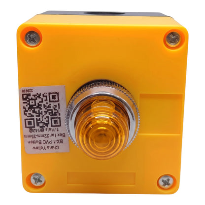 A square yellow plastic push-button switch with a central amber glass lens and a silver metal bezel. A white sticker with a QR code and product details is attached on the left side, and four screws secure the casing.