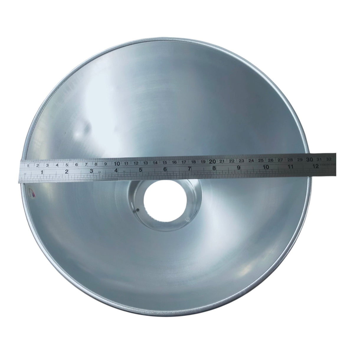 A silver metal spotlight reflector with a central mounting hole, shown with a metal ruler laid across the front to indicate its diameter.