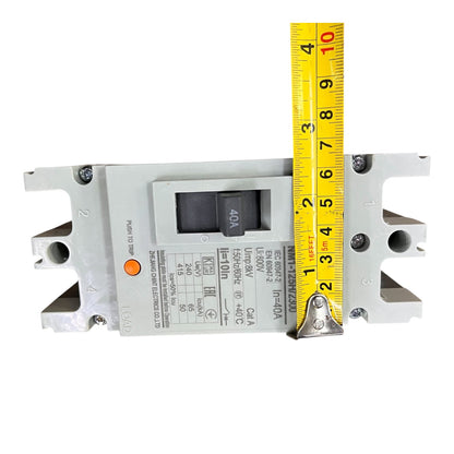A gray electrical circuit breaker shown on a white background with a yellow tape measure standing vertically next to it for scale.