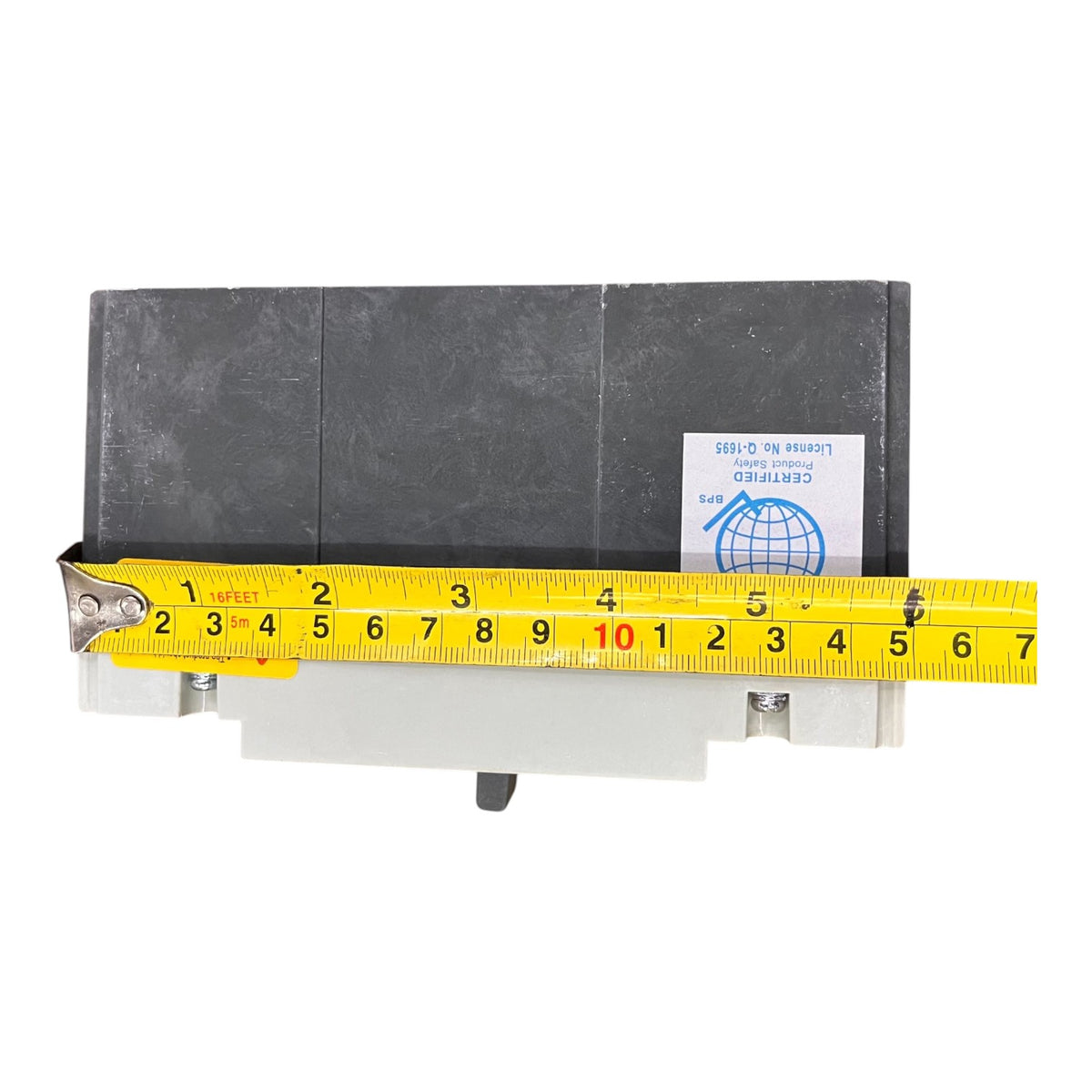 A rectangular black electronic component or module with a white base, shown on a white background with a yellow tape measure laid across the front to indicate dimensions. A small white certification sticker is visible on the right side.