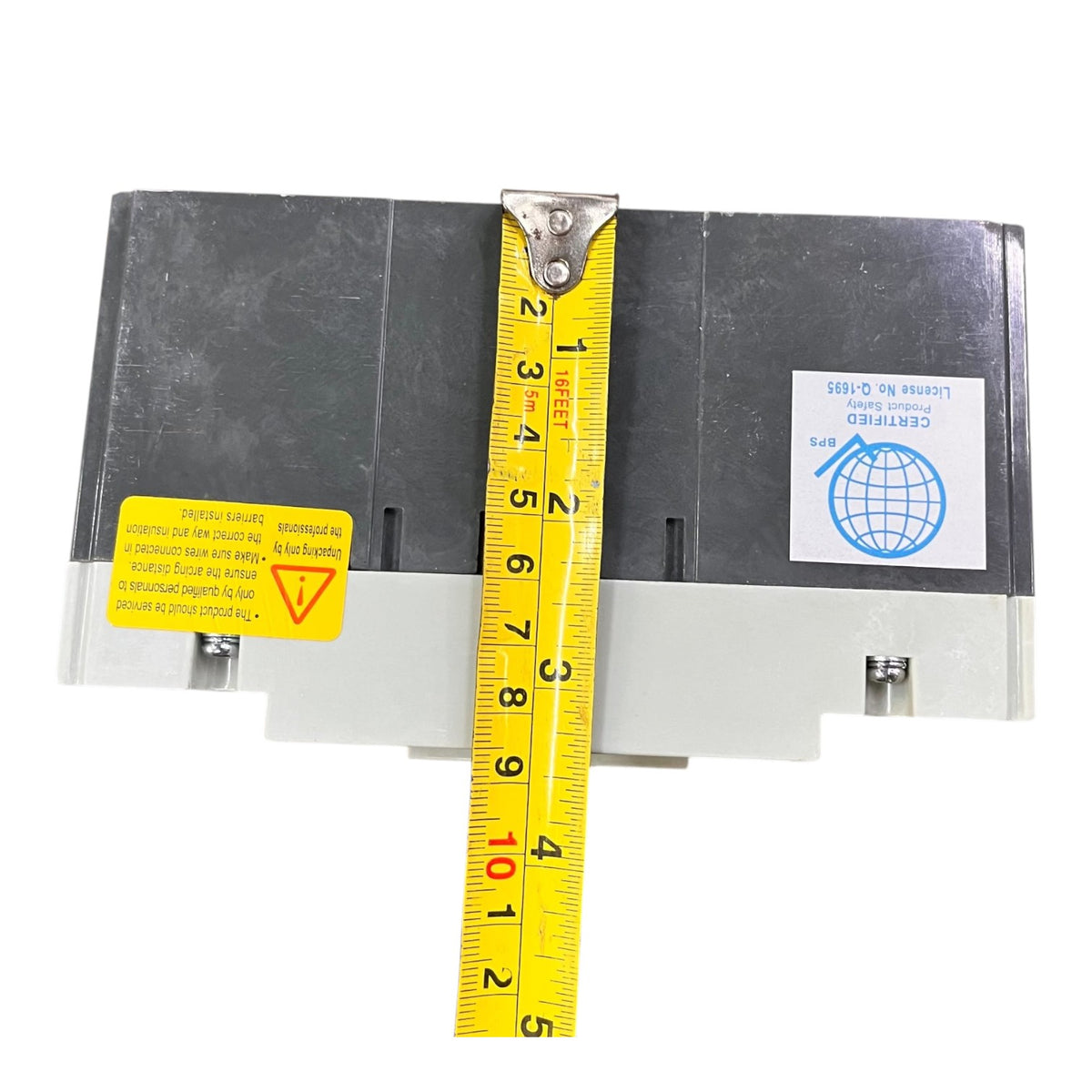A black industrial electrical component with a yellow tape measure stretched vertically across it to show dimensions, on a plain white background.