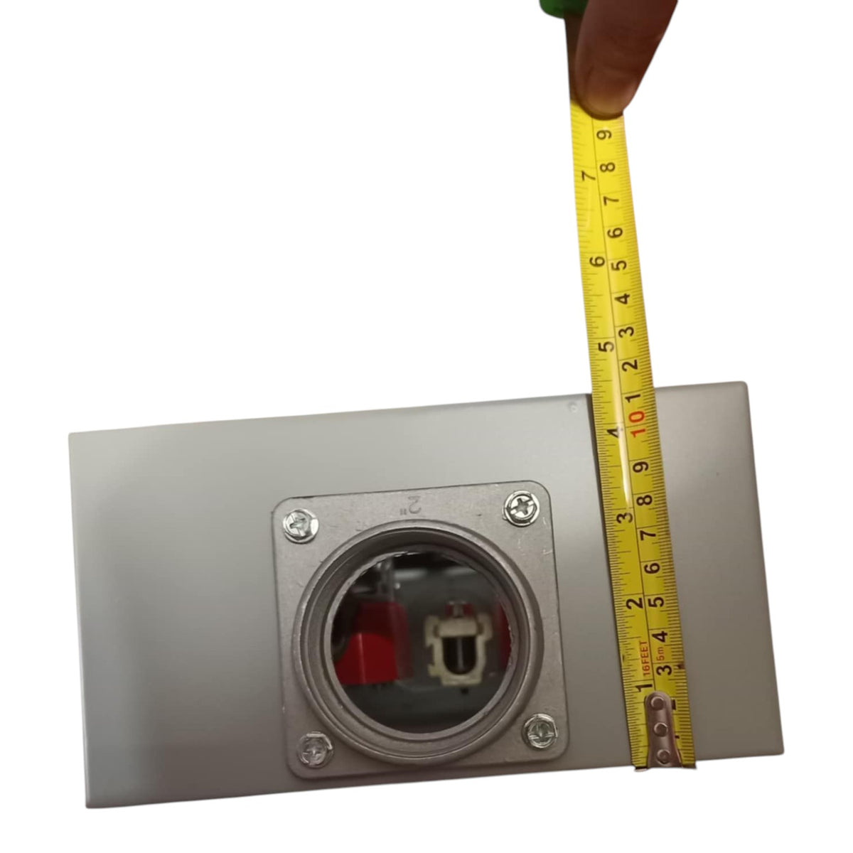 Metallic electrical outlet with a tape measure for scale on a white background