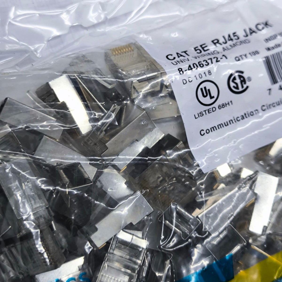 A clear plastic bag filled with many CAT 5E RJ45 Ethernet network jack connectors, with a white printed label showing model details and certification marks.