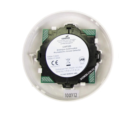 A Cooper CAP320 analogue addressable photoelectric smoke detector inside its white circular mounting base, showing the black and green electronic module with a white product label.