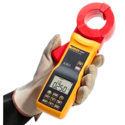 A Fluke multimeter clamp meter in yellow and red, held in a hand wearing a beige work glove against a solid white background.