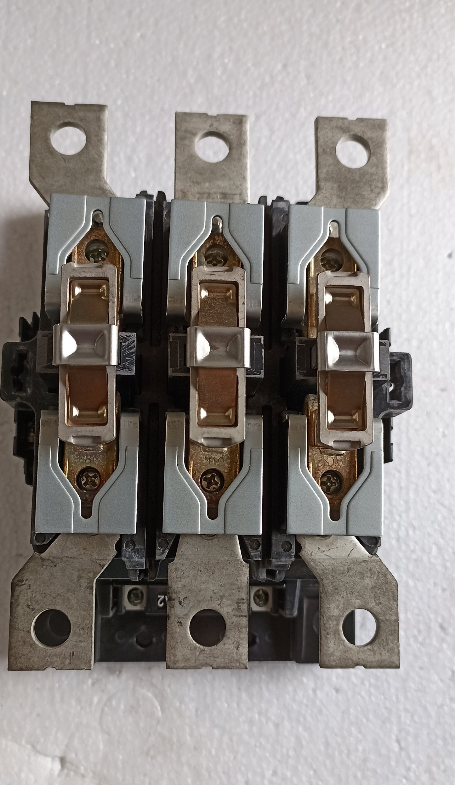 A three-pole electrical contactor or switch component with silver metal housings and copper-colored internal contacts, photographed against a white textured background.