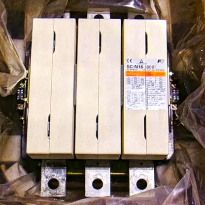 Three large beige industrial electrical contactors or relays stacked vertically, with a white technical label on the right unit. The units are photographed inside a cradle with protective plastic wrapping visible around them.