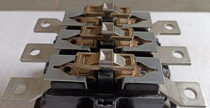 A close-up of a multi-contact electrical terminal block with silver metal plates, copper-colored spring contacts, and a black base on a light surface.