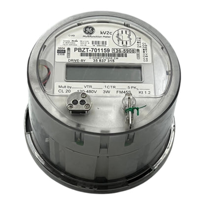 A GE 3-phase industrial digital watt-hour meter, model PBZT-701159, featuring a gray metal casing, a clear protective top cover, and an LCD display window.
