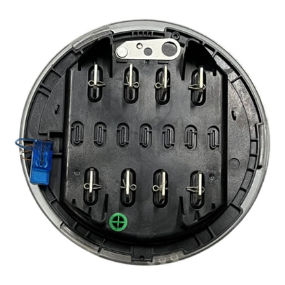 A circular black plastic battery compartment or terminal cover with multiple metal screw terminals, a blue wire connector on the left, and a green plus sign symbol near the bottom, shown on a white background.