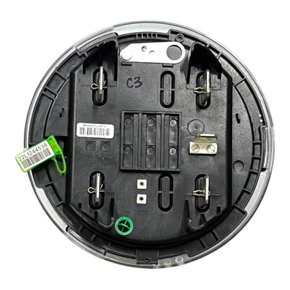 The underside of a circular electrical switch or control module, showing black molded plastic housing, metal terminal posts, a barcode label, a green plastic tag, and a green circular symbol on a white background.
