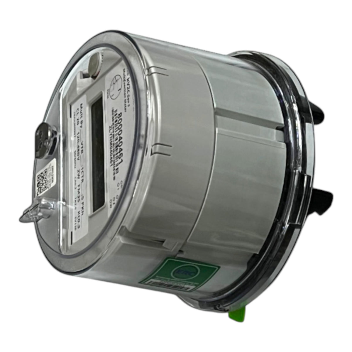 A digital electricity meter with a metallic silver body, clear protective casing, a digital display window, and a green safety label, shown on a plain white background.