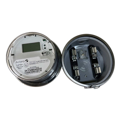 An open circular electrical meter showing the inside components, photographed on a plain white background. The left side shows the dial face with a small display and printed model text, and the right side shows the internal metal contacts and housing.