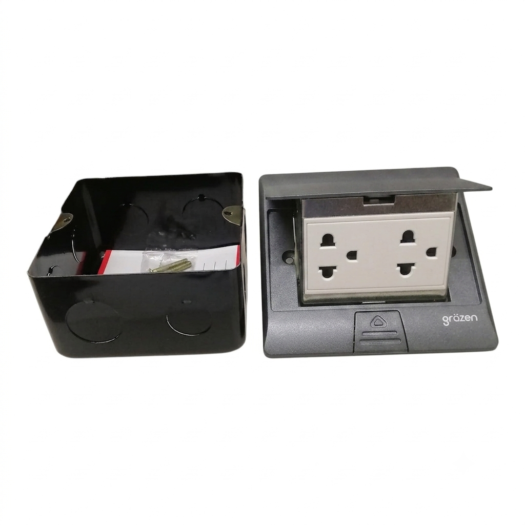 A black plastic electrical junction box shown next to its matching gray and black pop-up socket cover, which is open to reveal a double UK three-pin wall outlet. The brand name 'grozen' is visible on the lower right of the socket cover.