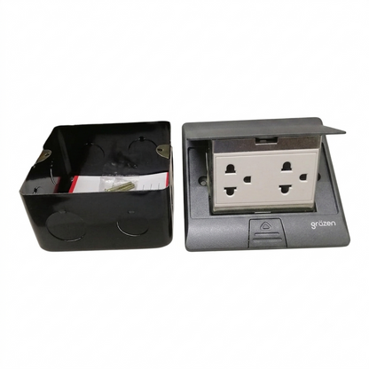 A black plastic electrical junction box shown next to its matching gray and black pop-up socket cover, which is open to reveal a double UK three-pin wall outlet. The brand name 'grozen' is visible on the lower right of the socket cover.