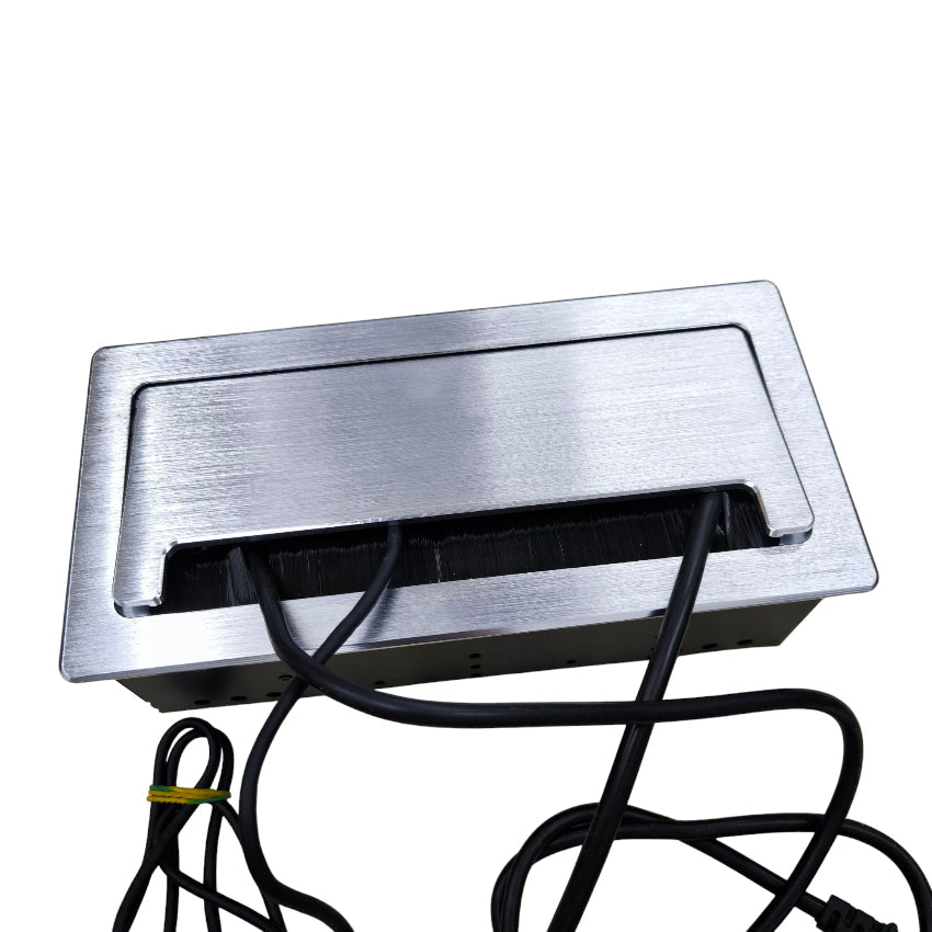 A brushed stainless steel under-cabinet electrical outlet cover with a black cable slot and visible black power cords, shown on a plain white background.